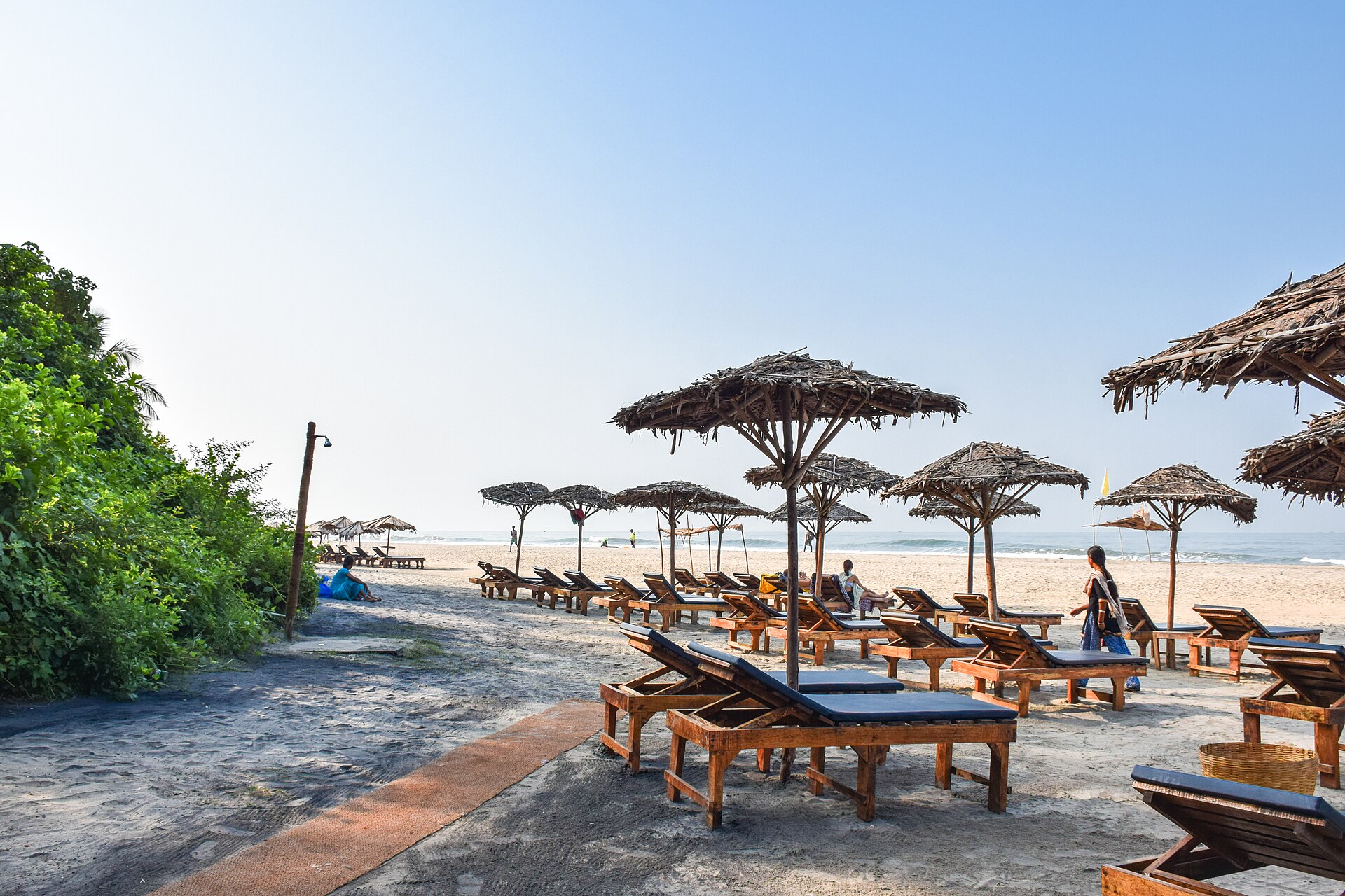 Broad silvery white sandy beach, gentle Arabian Sea waves, and coconut palm canopy at Ashwem Beach in Goa