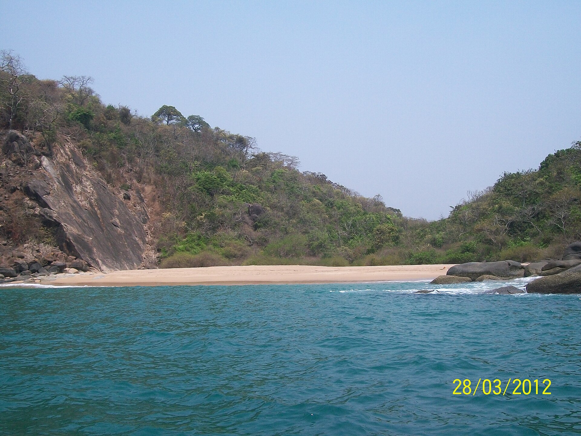 Secluded semi-circular turquoise bay and steep forested cliffs at Butterfly Beach in South Goa