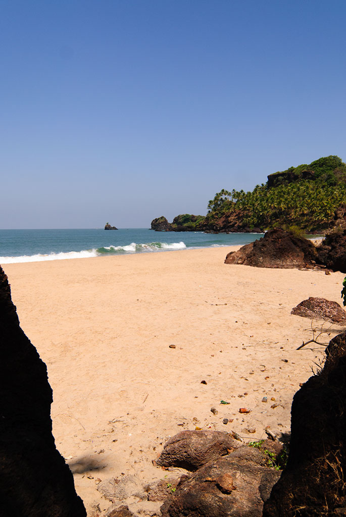 Secluded turquoise water pebble beach surrounded by laterite cliffs beneath Cabo de Rama Fort in South Goa