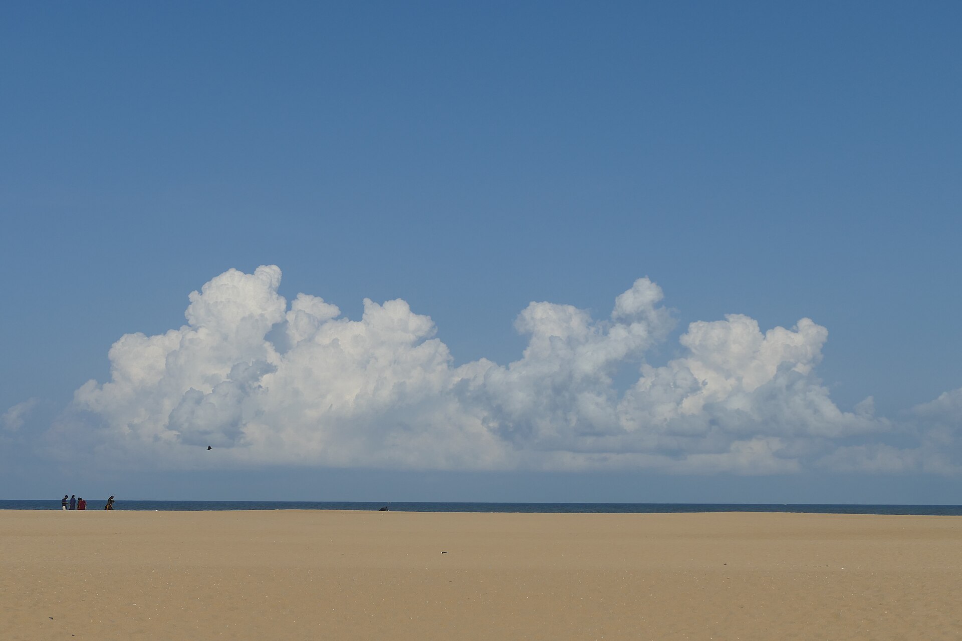 Dynamic coastal clouds over the golden sandy shoreline, wooden fishing catamarans, and rolling Bay of Bengal waves at Covelong Beach in Tamil Nadu