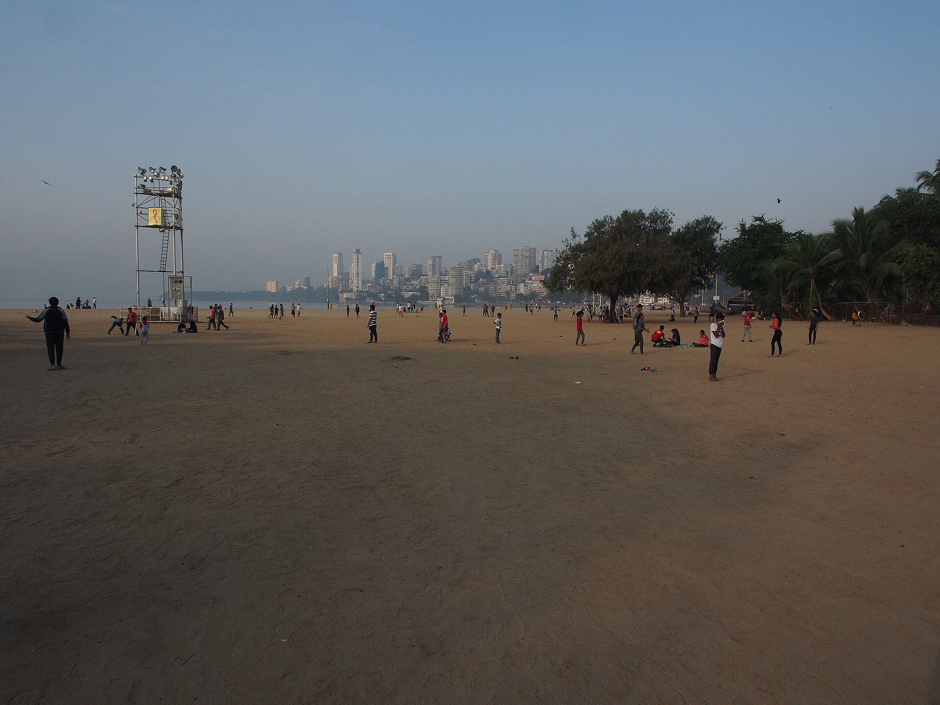 Broad sandy beach of Girgaon Chowpatty with Marine Drive promenade curving along Back Bay and Malabar Hill skyline in South Mumbai