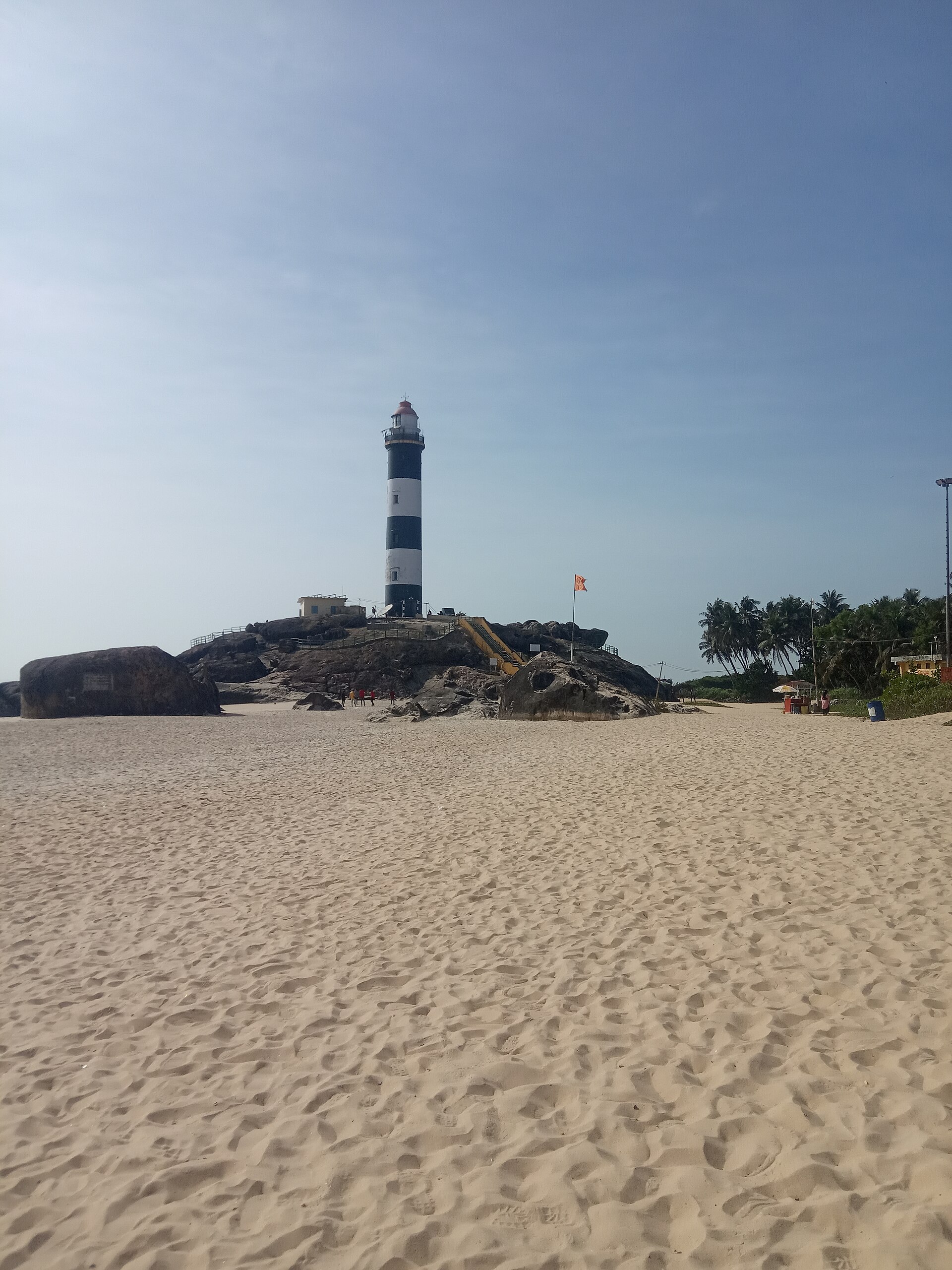 Historic 1901 lighthouse tower standing tall atop black granite rock boulders against the Arabian Sea at Kapu Beach in Udupi