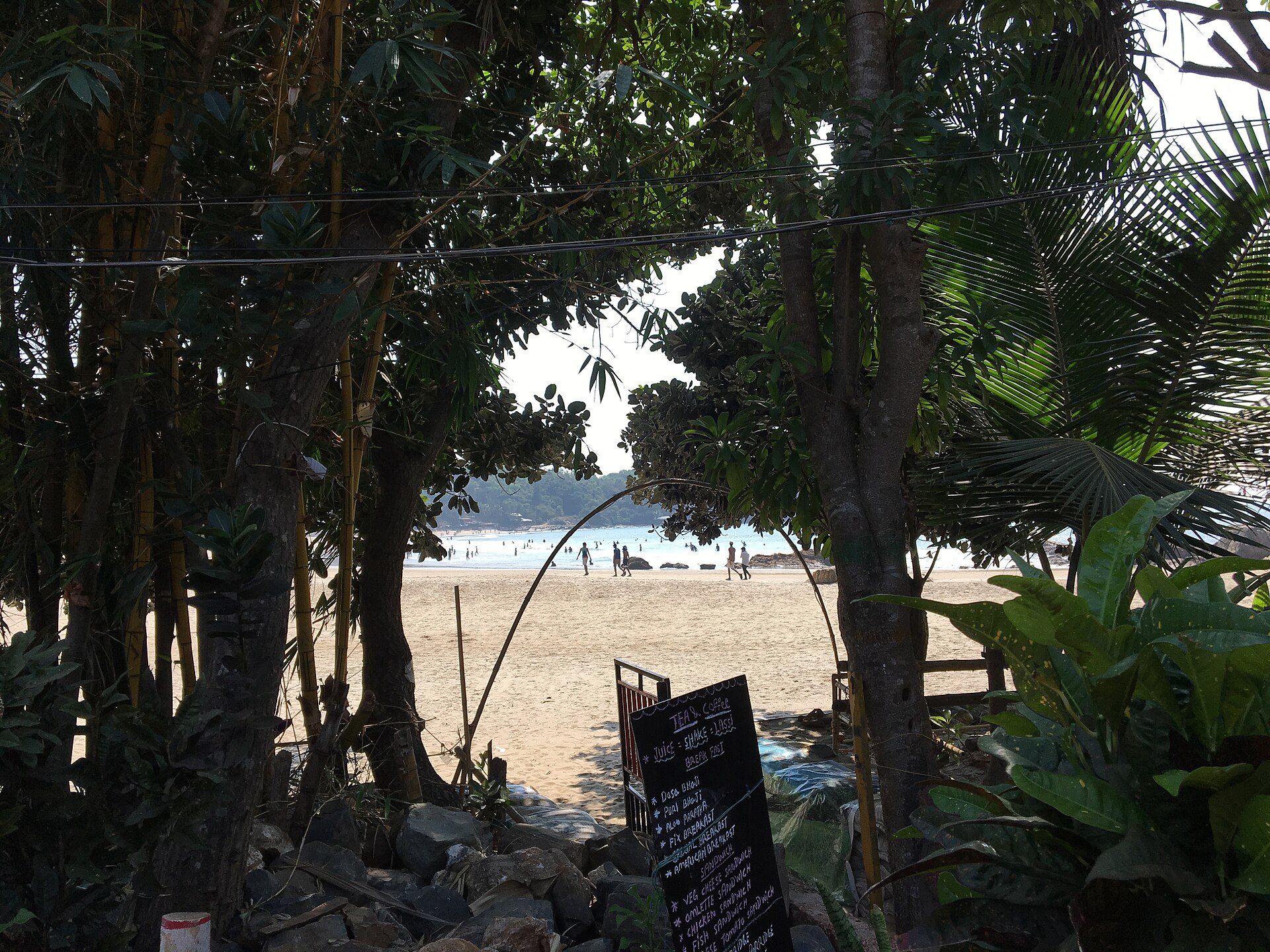 Broad sweeping crescent bay of Kudle Beach enclosed by crimson laterite headlands and palm groves in Gokarna, Karnataka