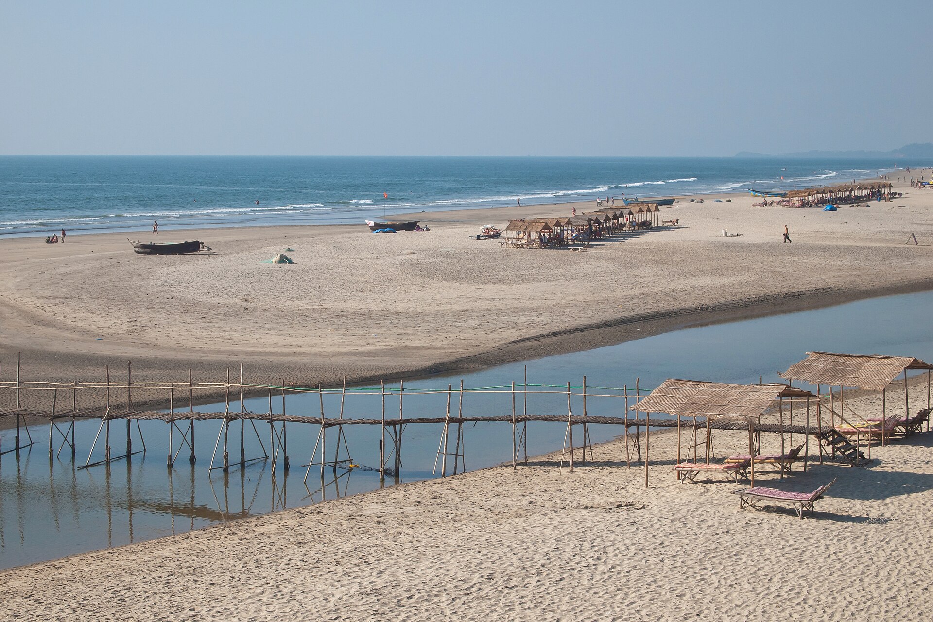 Scenic rustic wooden bridge crossing the Mandrem tidal river onto the vast golden sand beach in Goa