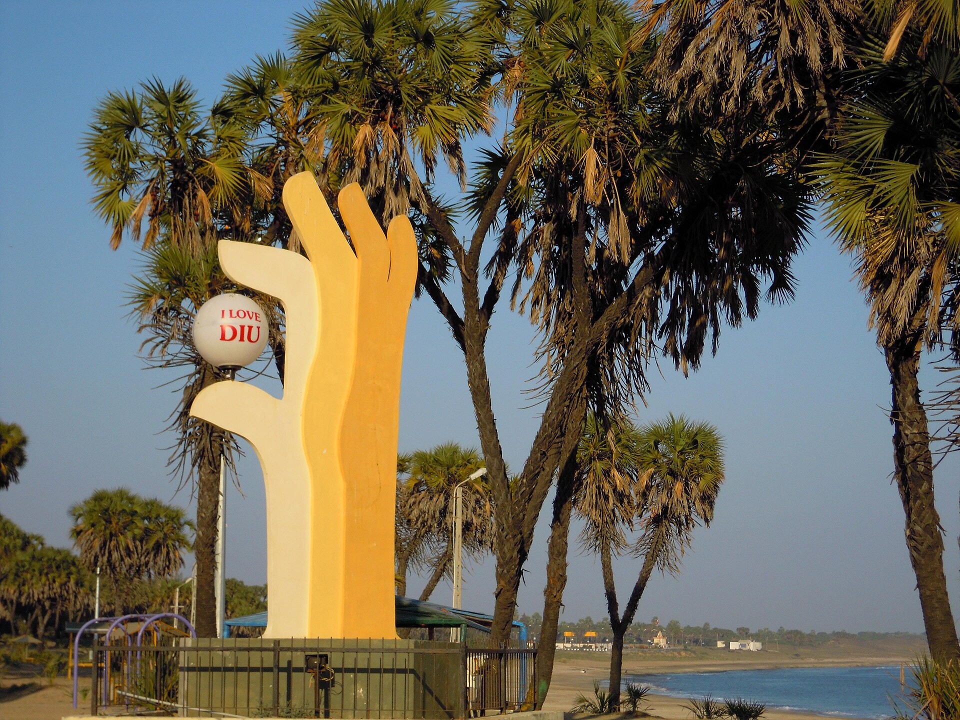 Curved semi-circular sandy bay, unique African Hoka palm trees, and calm turquoise Arabian Sea at Nagoa Beach in Diu