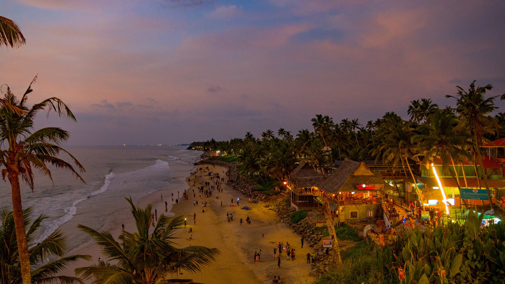 Towering red laterite cliffs of Varkala Beach overlooking golden sand and rolling waves of the Arabian Sea in Kerala